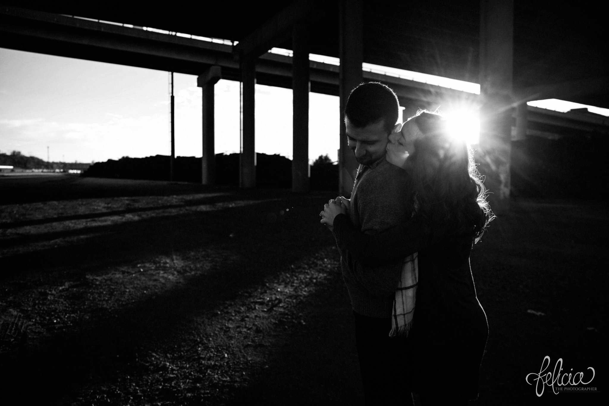 black and white | engagement photos | engagement photography | Kansas City | West Bottoms | images by feliciathephotographer.com | urban setting | industrial background | sun flare | romantic pose | kiss on cheek | sunset | holding hands | bridge background | downtown background | cuddling | engagement shoot 