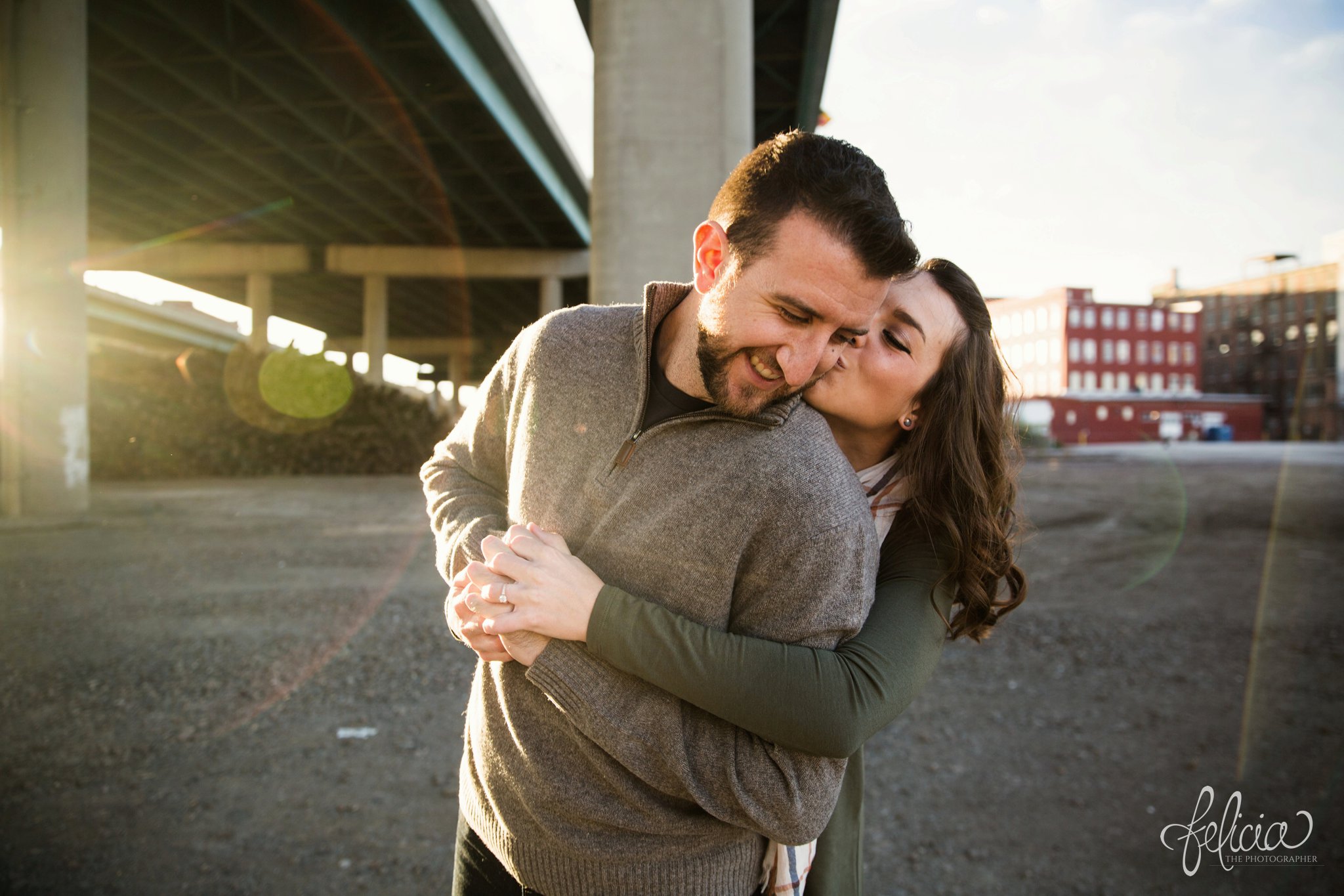 engagement photos | engagement photography | Kansas City | West Bottoms | images by feliciathephotographer.com | urban setting | industrial background | sun flare | romantic pose | kiss on cheek | holding hands | bridge background | downtown background 