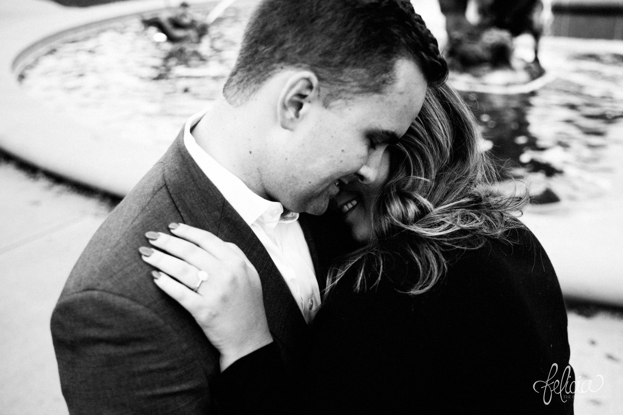 black and white | engagement photos | engagement photography | Kansas City | images by feliciathephotographer.com | architectural backgrounds | downtown | downtown Kansas City | fountain | hands on shoulders | engagement ring | circle cut | closed eyes | romantic pose | cuddling 