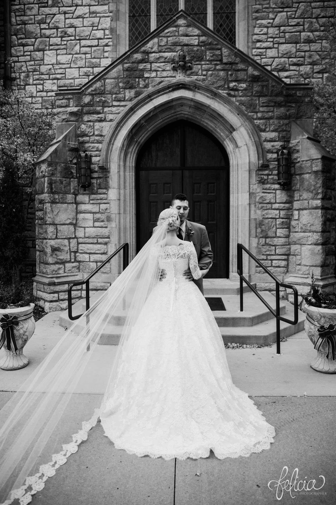 black and white | wedding | wedding photography | wedding photos | Kansas City | St. Patrick's Catholic Church | Hawthorne House | images by feliciathephotographer.com | crimson wedding | Christmas Wedding | winter portraits | dramatic veil | lace sleeves | lace wedding dress | Paula Varsalona | bride and groom | embrace | church doors | back to camera 