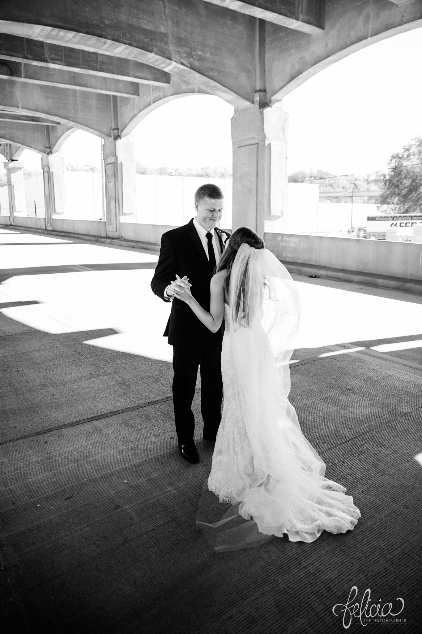 black and white | wedding | wedding photos | industrial | Rumely Event Space | wedding photography | images by feliciathephotographer.com | West Bottoms | first look | Maggie Sottero | bride and groom | industrial background | linking hands | candid