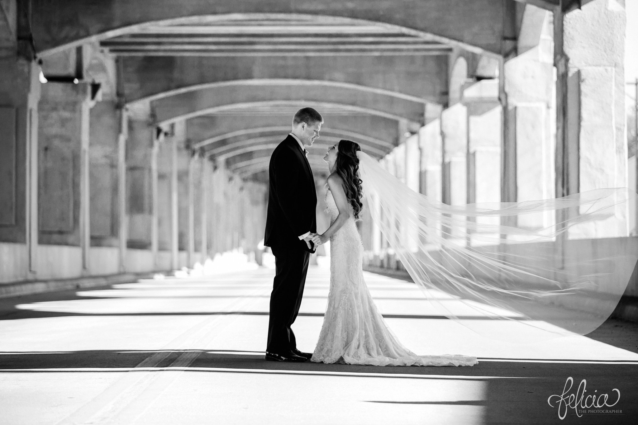 black and white | wedding | wedding photos | industrial | Rumely Event Space | wedding photography | images by feliciathephotographer.com | West Bottoms | first look | Maggie Sottero | bride and groom | industrial background | linking hands | candid | profile | flowing veil | dramatic | long veil 
