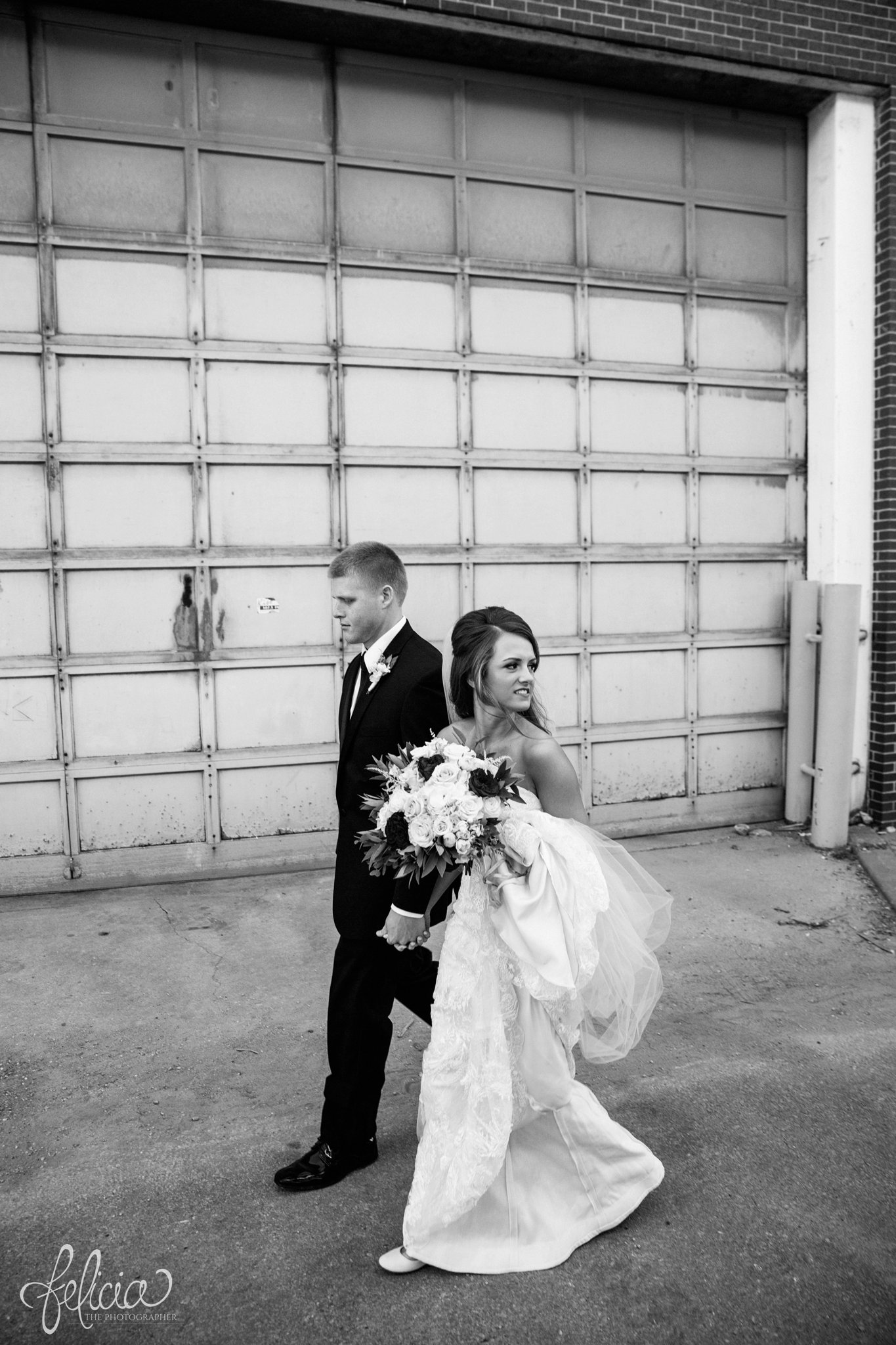 black and white | wedding | wedding photos | industrial | Rumely Event Space | wedding photography | images by feliciathephotographer.com | West Bottoms | industrial background | garage | candid | walking | hand in hand 
