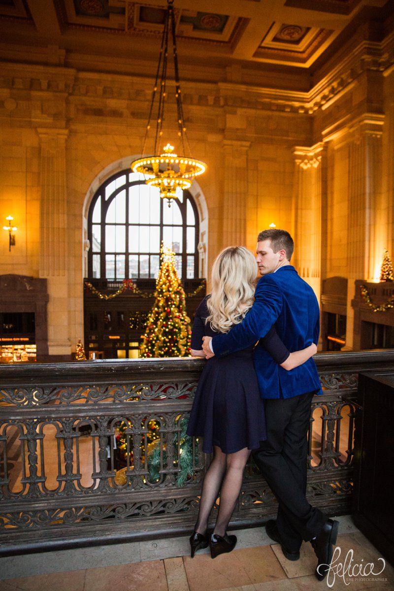 engagement photos | night engagement photos | Union Station | Kansas City | images by feliciathephotographer.com | romantic engagement | hugging pose | dramatic background | scallop neck dress | pearl accessories | blue blazer | romantic poses | chandelier | Old Hollywood | Christmas engagement photos | high ceilings | embracing 