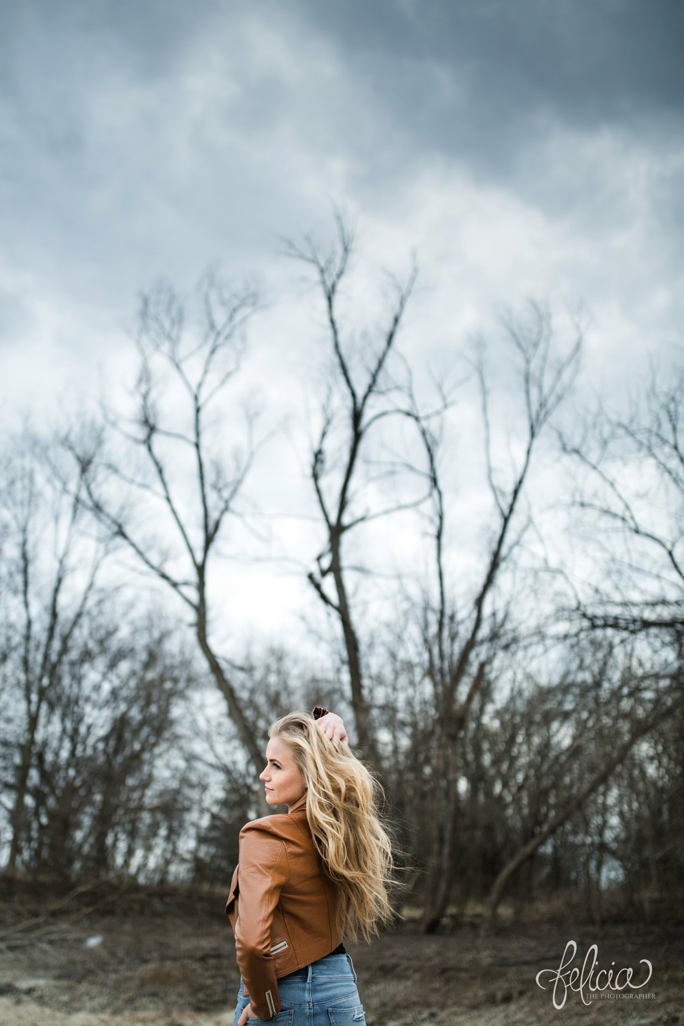 senior photos | senior photography | Lenexa | Kansas | images by feliciathephotographer.com | chic | dancer | dramatic pose | leather jacket | rustic background | forest background | long blonde hair | hand on hip | hand in hair 