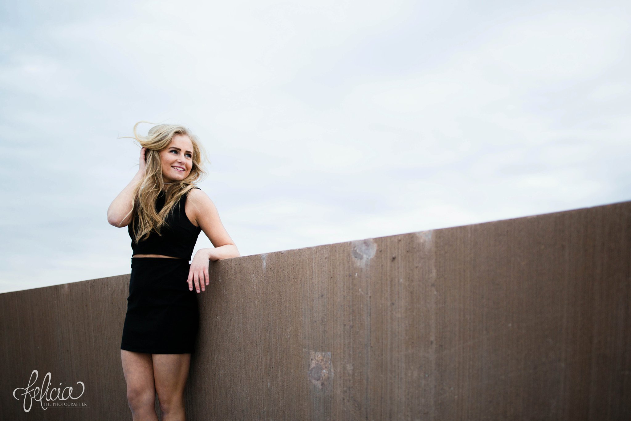 senior photos | senior photography | Lenexa | Kansas | images by feliciathephotographer.com | chic | dancer  | long blonde hair | hair flip | pearl jewelry | pearl necklace | pearl earrings | black outfit | dramatic pose | smiling | hand in hair | full body | leaning against wall  