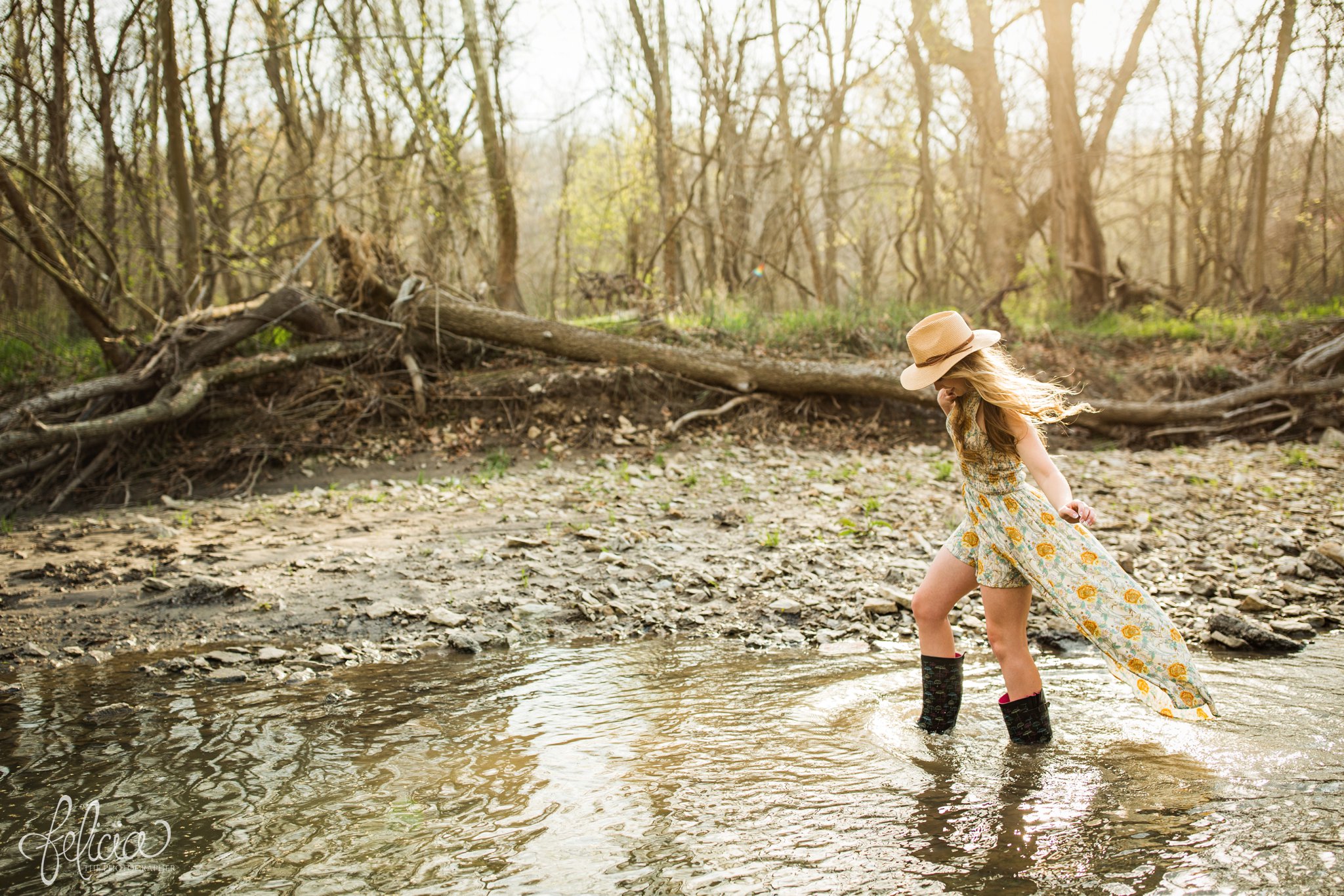 senior pictures | images by feliciathephotographer.com | Kansas City | rustic | long blonde hair | nature background | trees | flower print dress | yellow dress | fedora hat | senior pictures in water | rain boots | candid 