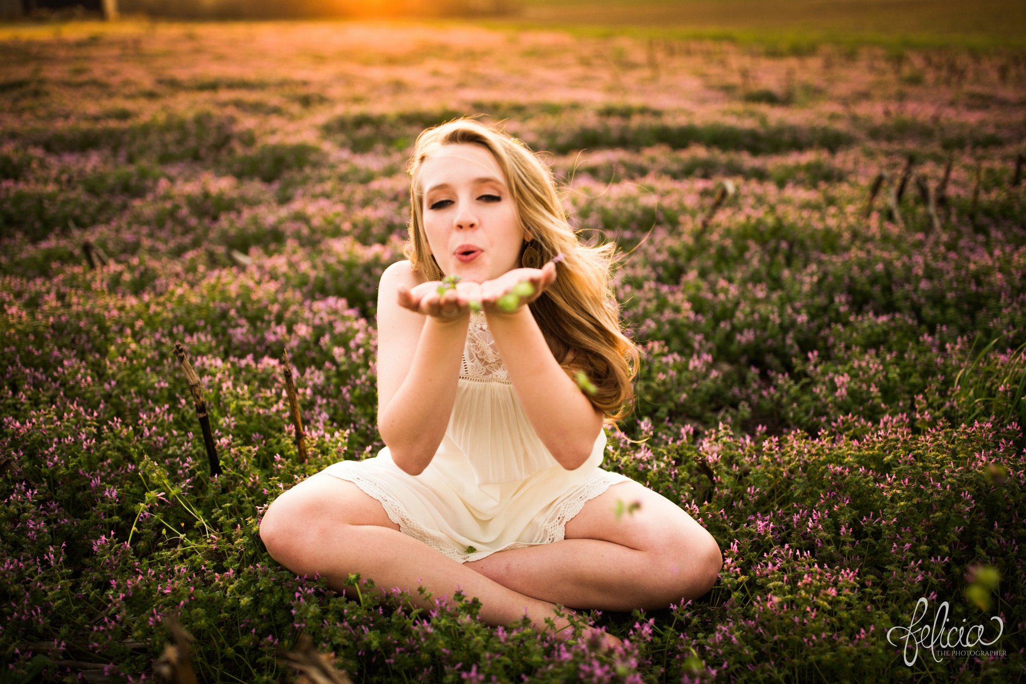 senior pictures | images by feliciathephotographer.com | Kansas City | rustic | long blonde hair | nature background | white dress | elegant | dramatic | candid | dramatic pose | flower field | sitting in flowers | cross legged | purple flowers | blowing kisses 