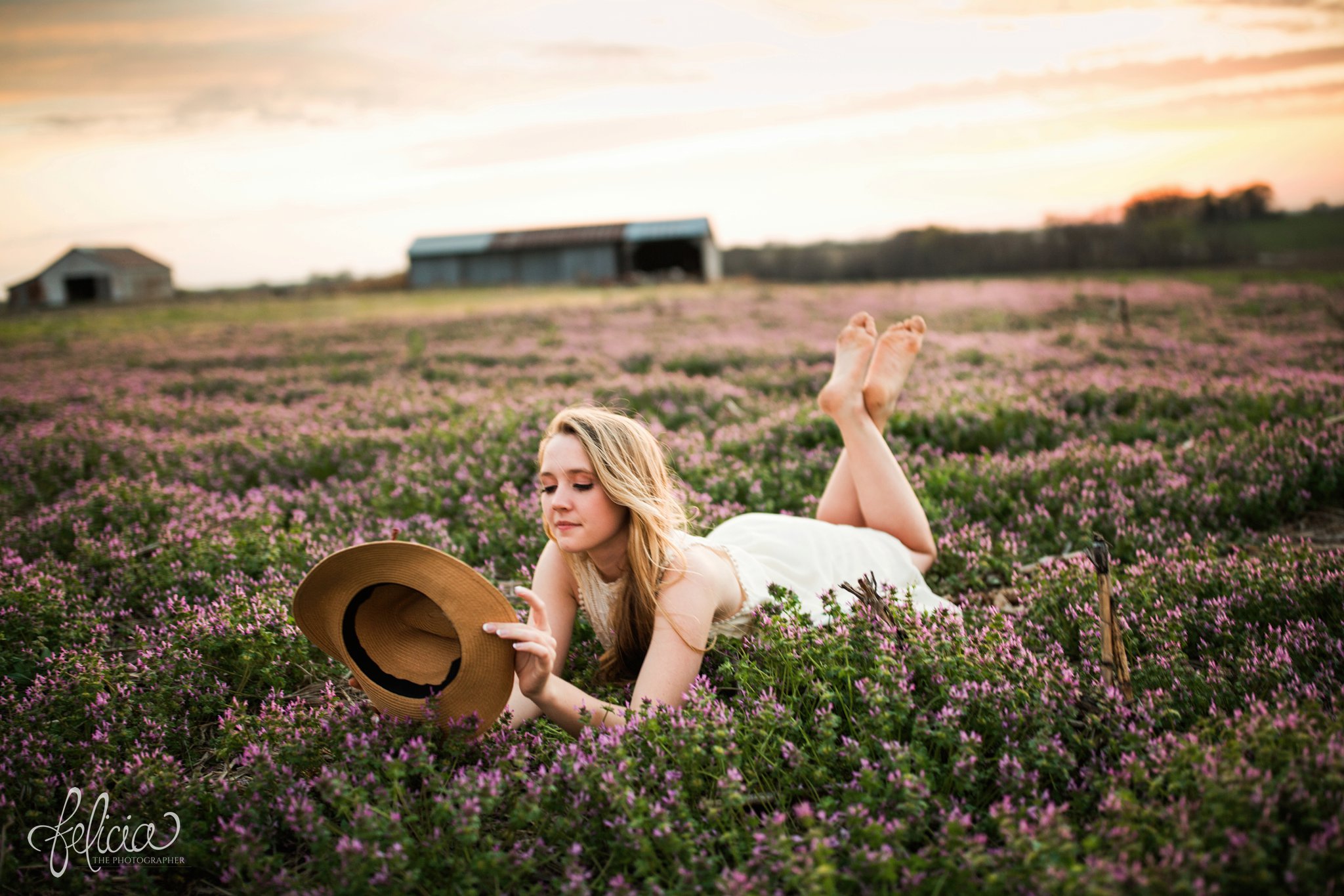 senior pictures | images by feliciathephotographer.com | Kansas City | rustic | long blonde hair | nature background | white dress | elegant | dramatic | candid | dramatic pose | flower field | sitting in flowers | purple flowers | lying in field | fedora hat | sunset | farm house 