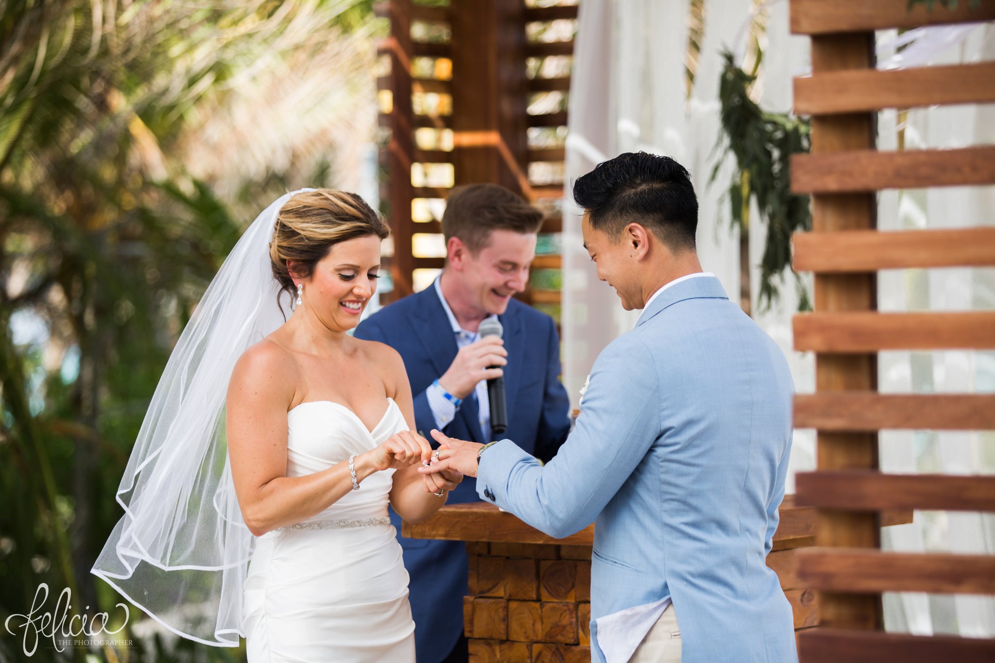 images by feliciathephotographer.com | Destination Beach Wedding | Unicco 20 87 | Photographer | L&S Travel | ceremony | stone altar | wooden gazebo | white tule | blue jacket | strapless dress | up-do veil | pastor | palm trees | ocean | laughter | joy | exchanging rings | saying vows 