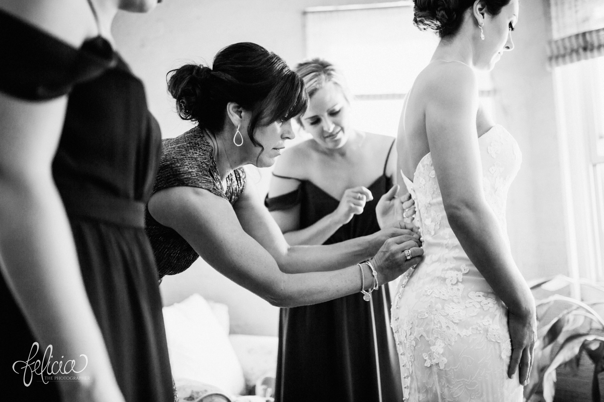 images by feliciathephotographer.com | wedding photographer | kansas city | getting ready | putting on the dress | bridesmaids | buttons | lace floral dress | strapless | emily hart | black and white | 