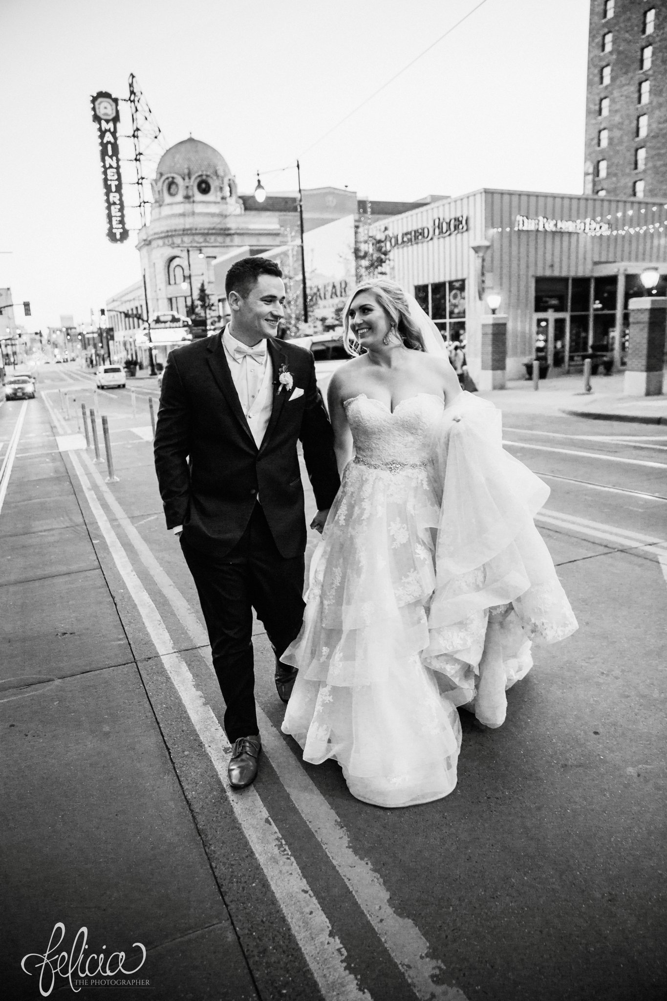 images by feliciathephotographer.com | wedding photographer | downtown kansas city | bride and groom candid | middle of the street | urban | black and white | power and light | romantic | holding hands | lace dress | belle vogue | black suit | men's warehouse | 