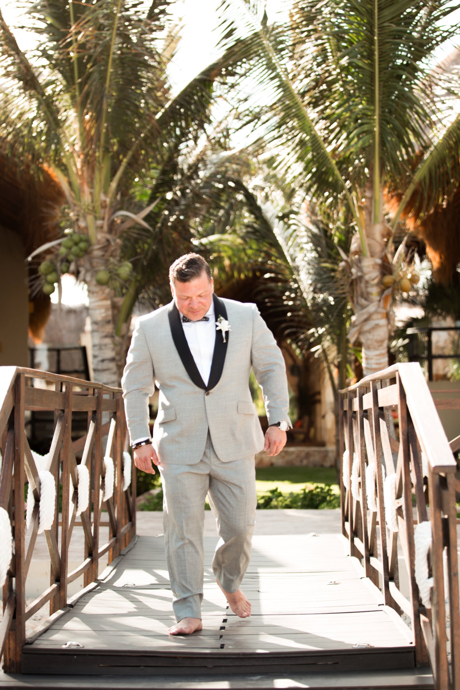  images by feliciathephotographer.com | destination wedding photographer | mexico | tropical | fiji | venue | azul beach resort | riviera maya | groom | ceremony | walking down the aisle | barefoot | grey suit | bow tie | palm trees | 