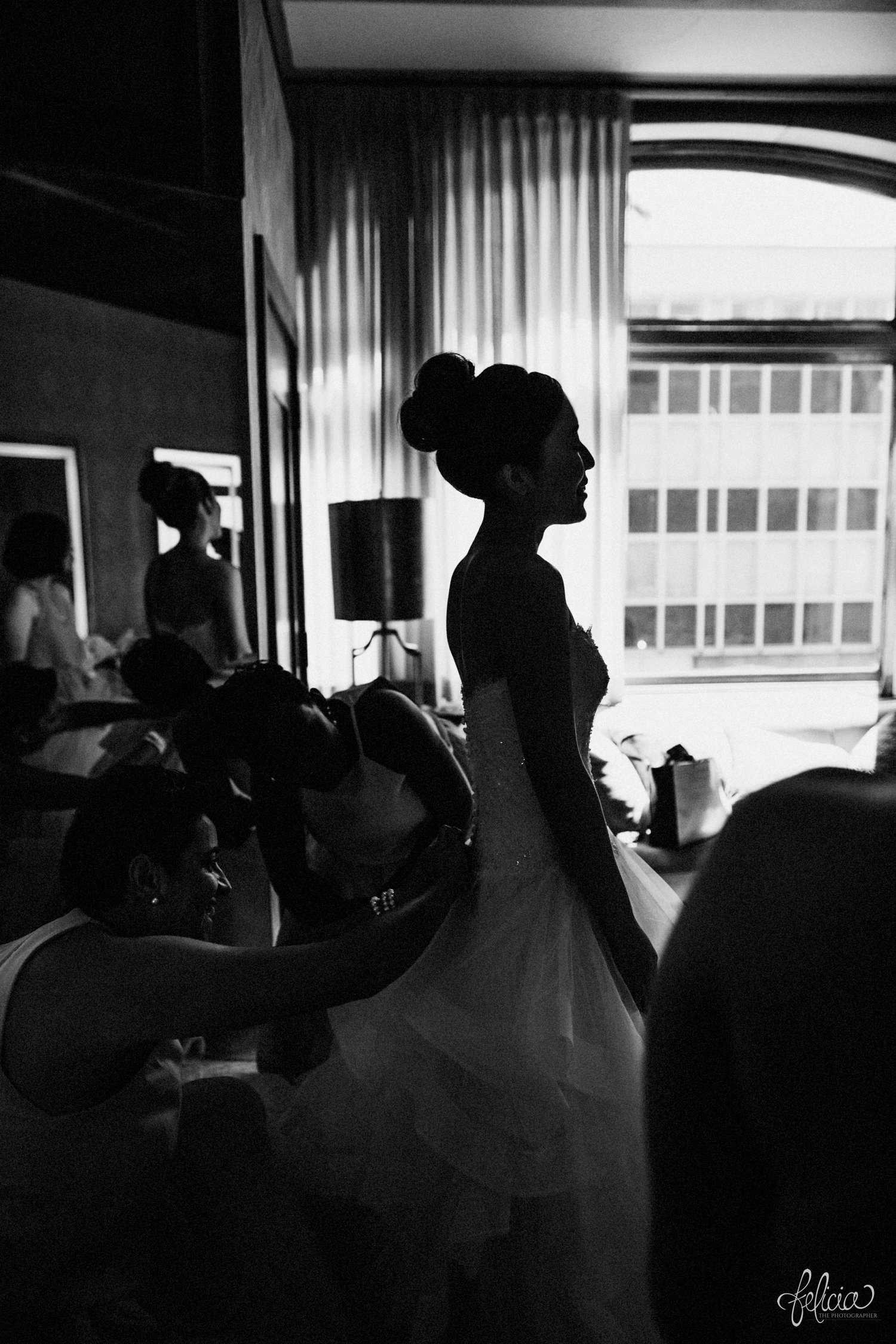 images by feliciathephotographer.com | destination wedding photographer | the grand hall at power and light | kansas city | missouri | downtown | glamorous | multicultural | getting ready | putting on the dress | details | black and white | posh bridal | high bun | strapless | dramatic lighting | 