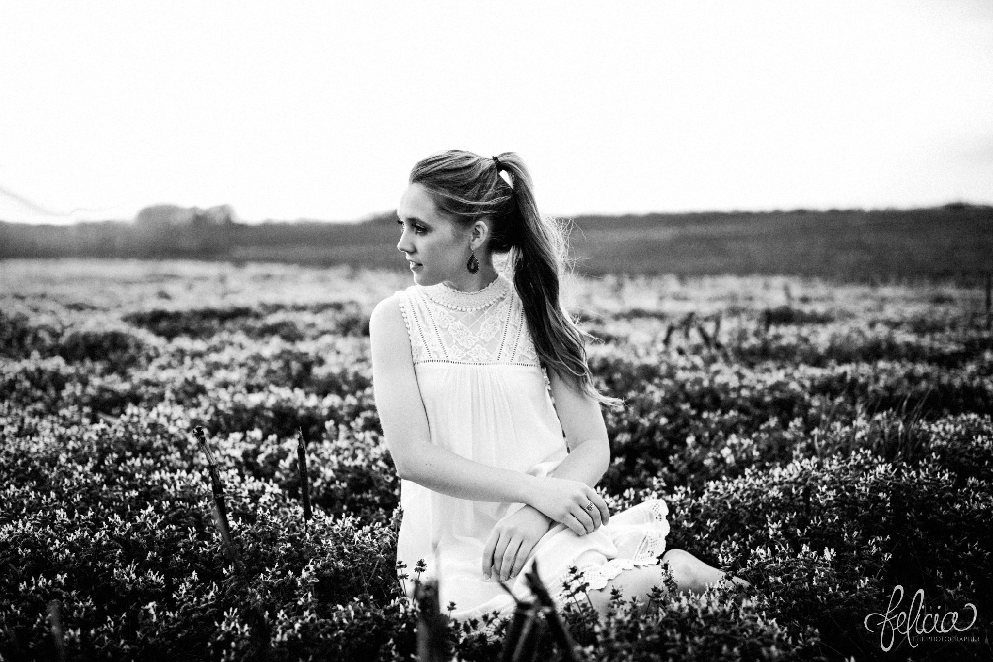 black and white | senior pictures | images by feliciathephotographer.com | Kansas City | rustic | long blonde hair | nature background | white dress | elegant | dramatic | candid | dramatic pose | ponytail | flower field | sitting in flowers 